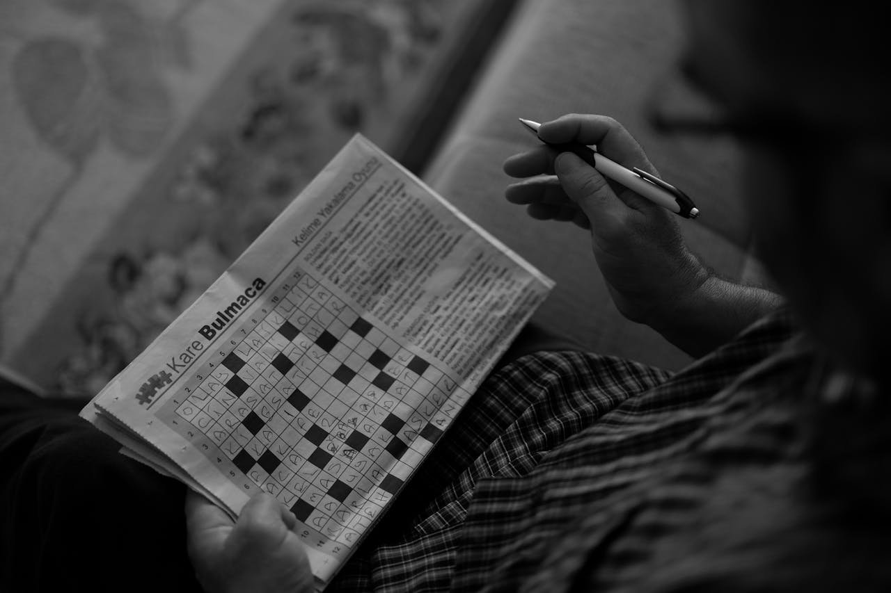 A person solving a monochrome crossword puzzle indoors, using a pen.